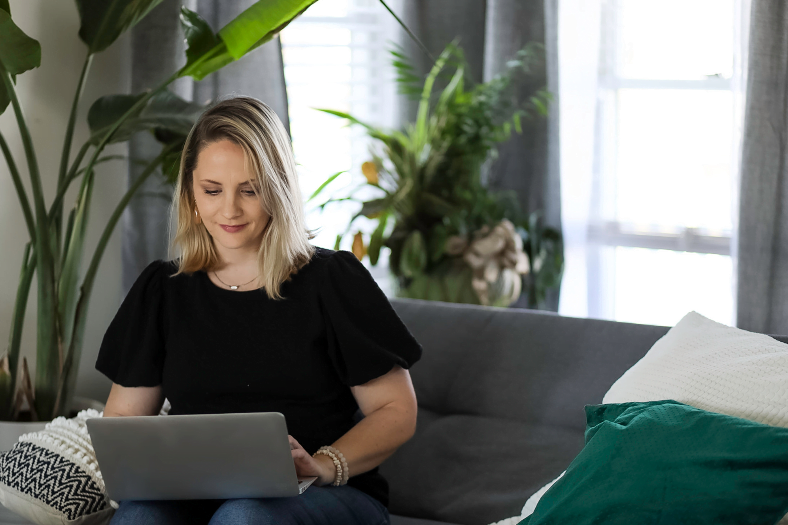 Artistic young woman sitting at a desk with a laptop and mug and fresh potted plants