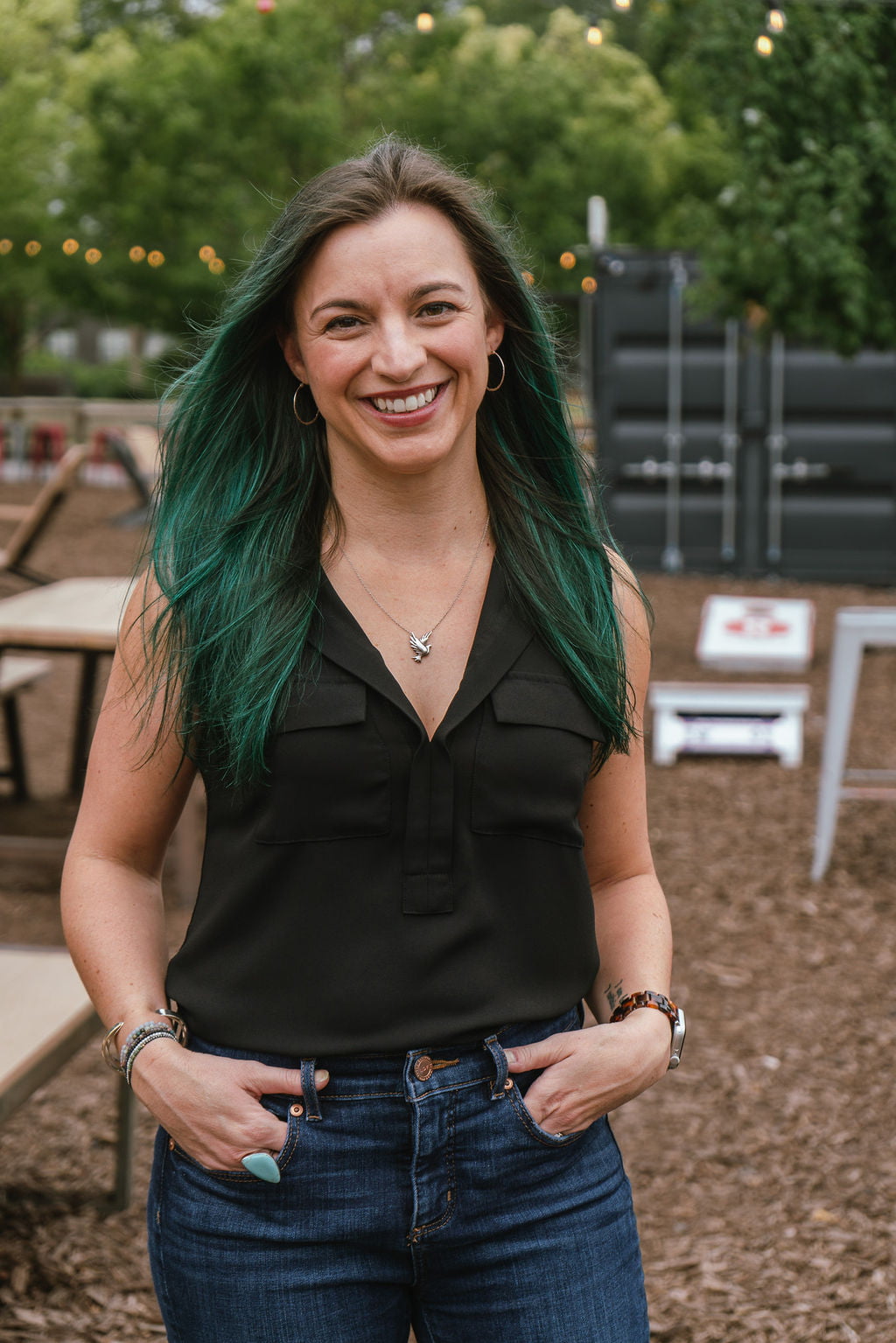 Young woman smiling at camera with hands in pockets and standing outside