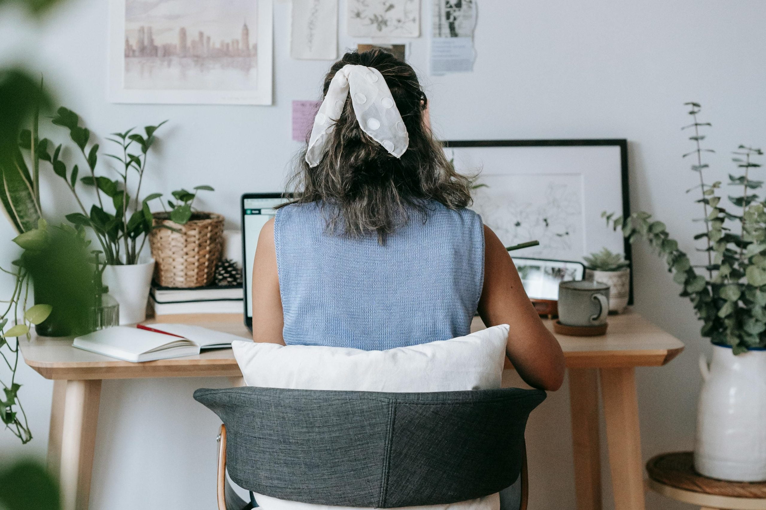 Female entrepreneur sitting at desk Artistic young woman sitting at a desk with a laptop and mug and fresh potted plants